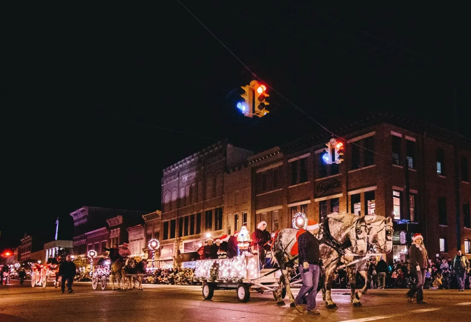 People gathered along illuminated storefronts in downtown Greenville at night.